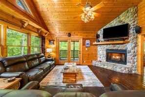 Relax in this inviting living room with a stone fireplace, leather sofa, and mounted television.