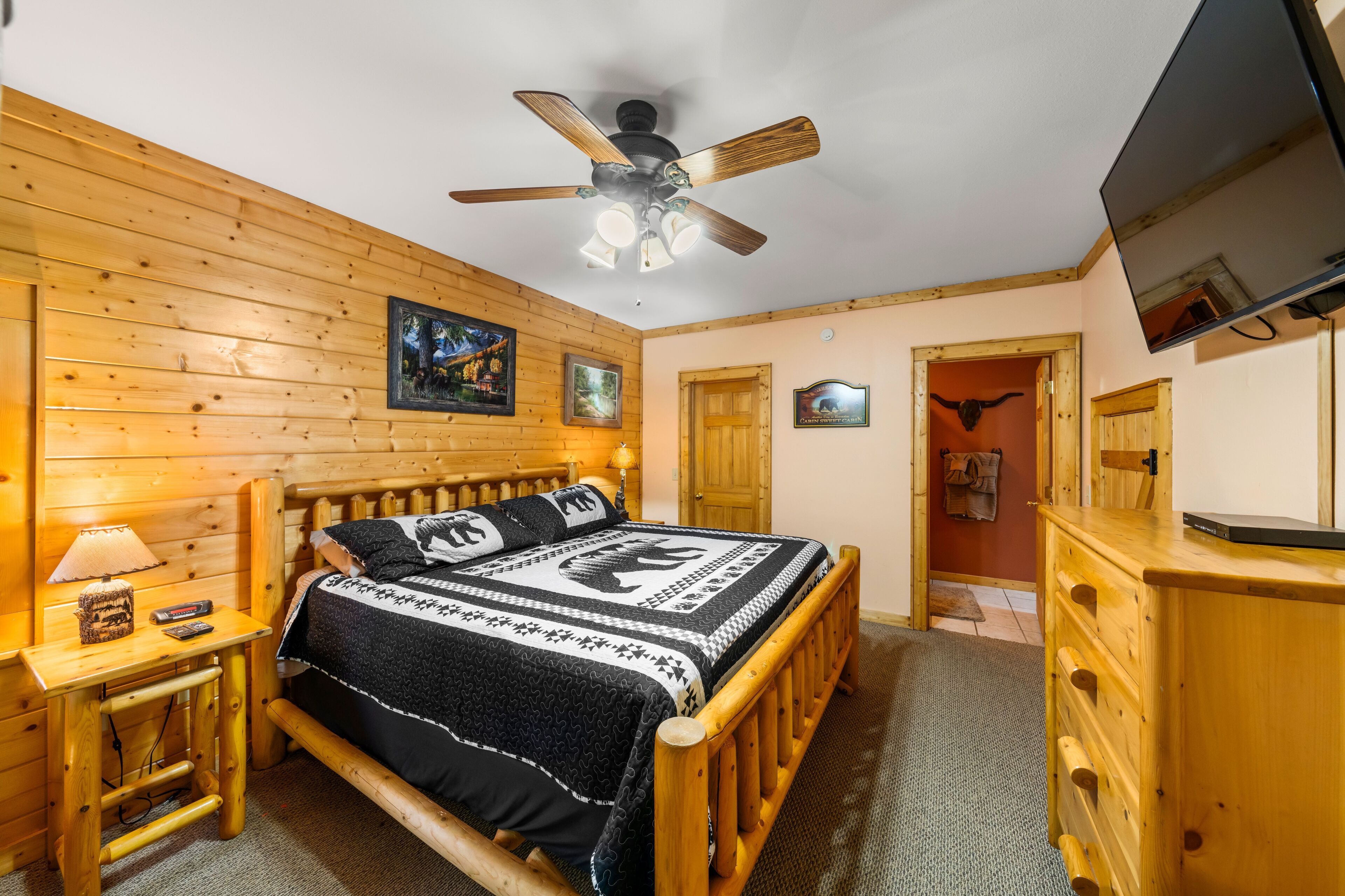 A wooden-paneled bedroom with a bed, a ceiling fan, a TV, and a wooden dresser.