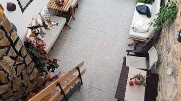 Un espacio al aire libre acogedor con bancos y mesas de madera, rodeado de plantas en macetas y un muro de piedra.