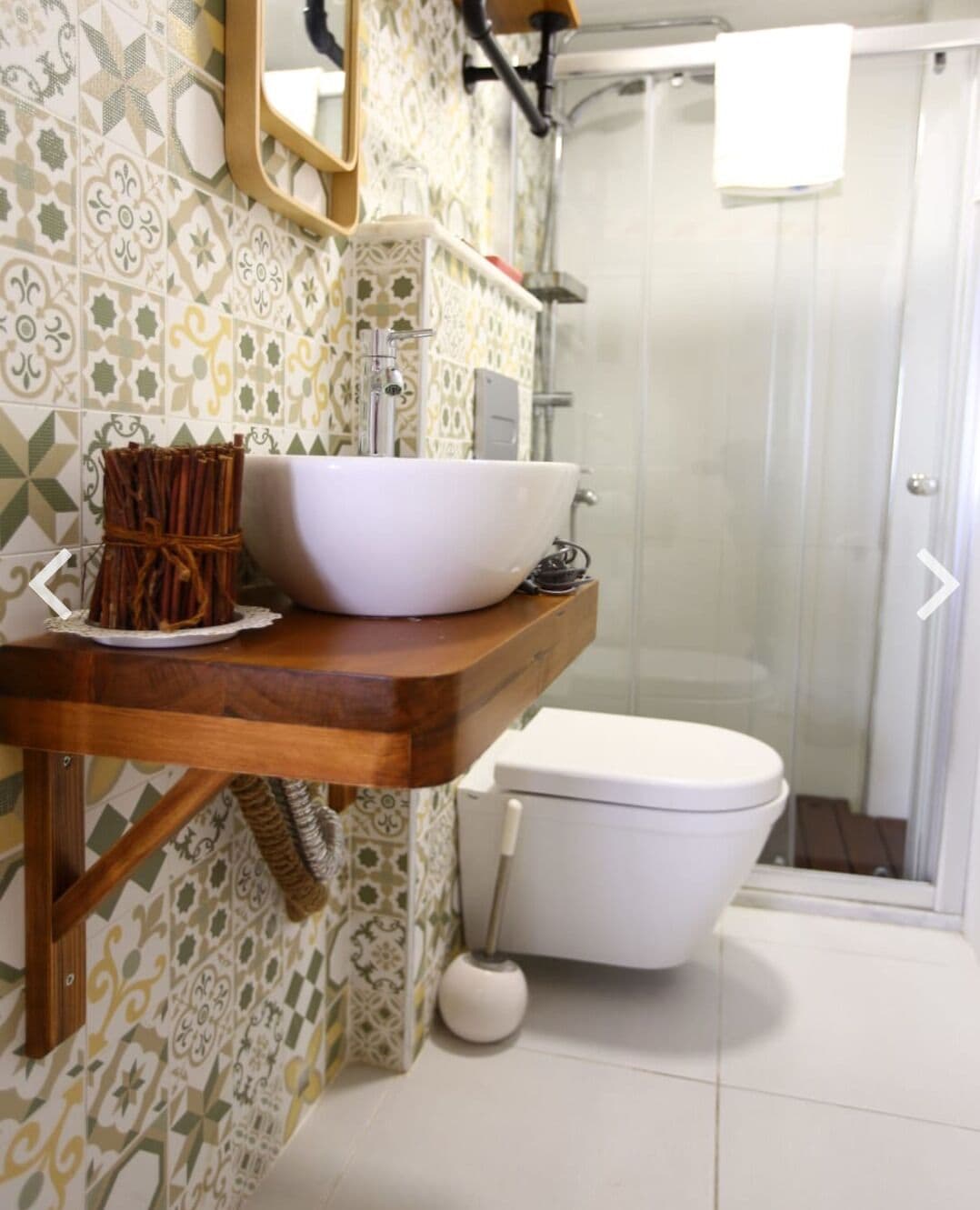 A bathroom with a white toilet, a wooden vanity with a white basin, and patterned tiles on the walls.