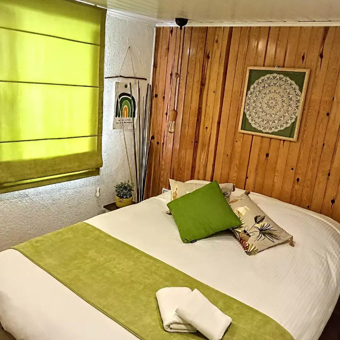 A neatly made bed with a green throw, a decorative pillow, and a folded towel on a white bedspread.