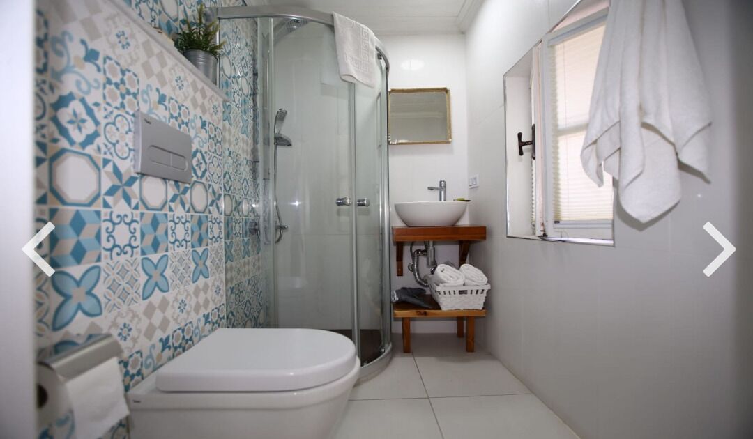 Un baño con ducha, inodoro, lavamanos y una pequeña ventana, donde se ve una toalla colgada en la pared.