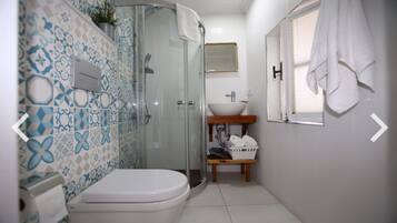 Un baño con ducha, inodoro, lavamanos y una pequeña ventana, donde se ve una toalla colgada en la pared.