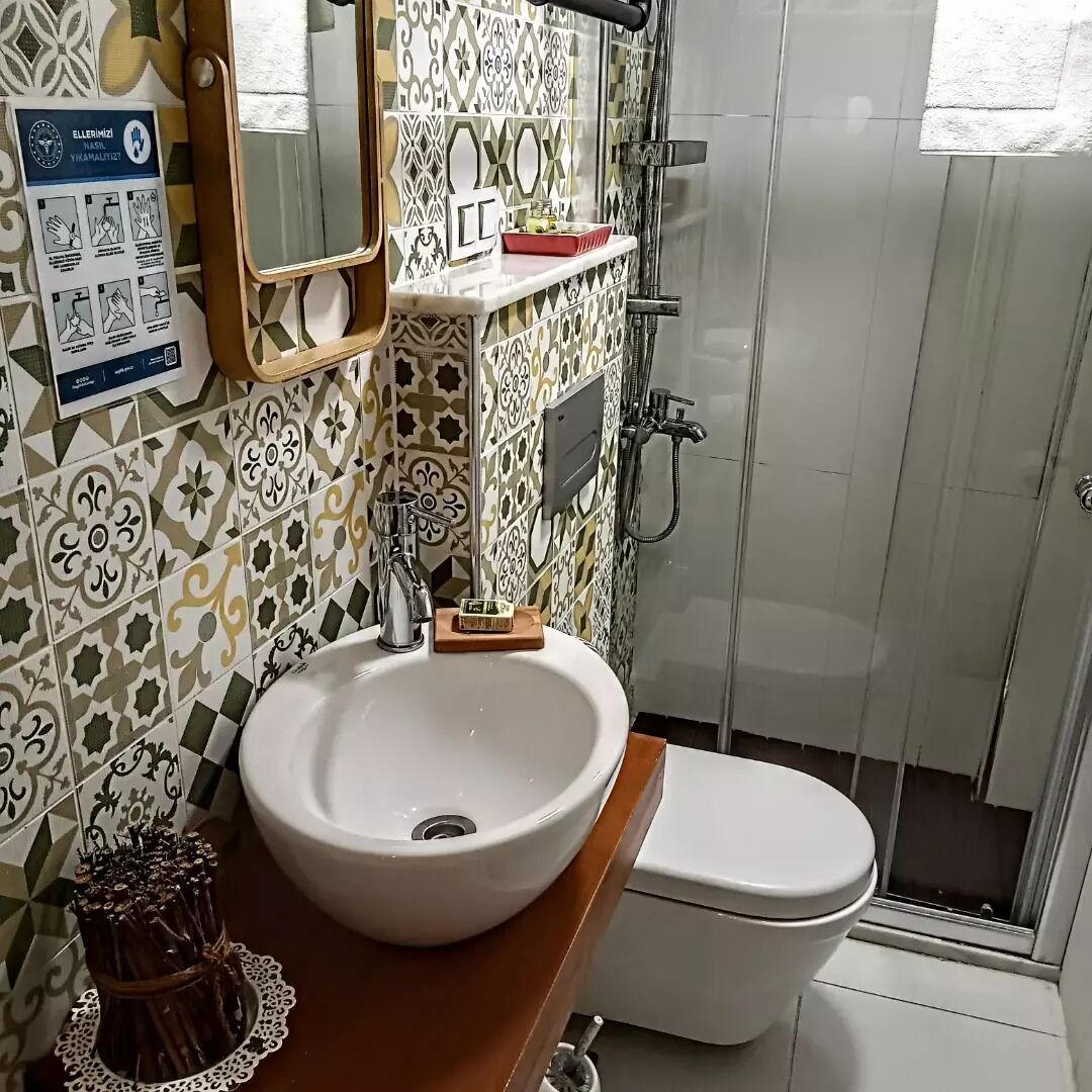 A bathroom with a white sink, a mirror, a shower, and a toilet. There is a poster on the wall with hygiene instructions.