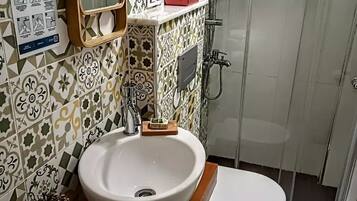 A bathroom with a white sink, a mirror, a shower, and a toilet. There is a poster on the wall with hygiene instructions.