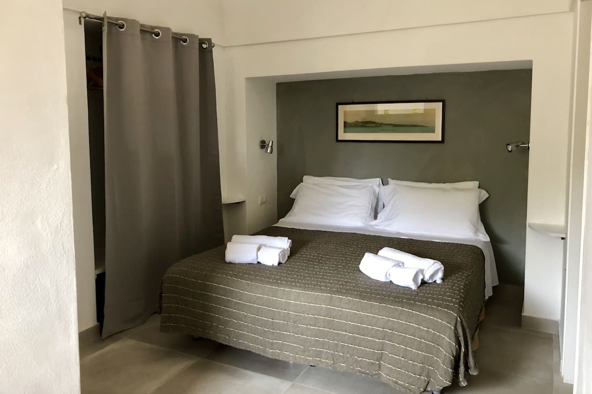 A neatly made bed with white pillows and towels, a grey striped bedspread, and a framed picture on the wall above the bed.