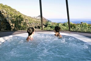Un jacuzzi con dos personas, rodeado de una vista panorámica de un promontorio rocoso y el océano.