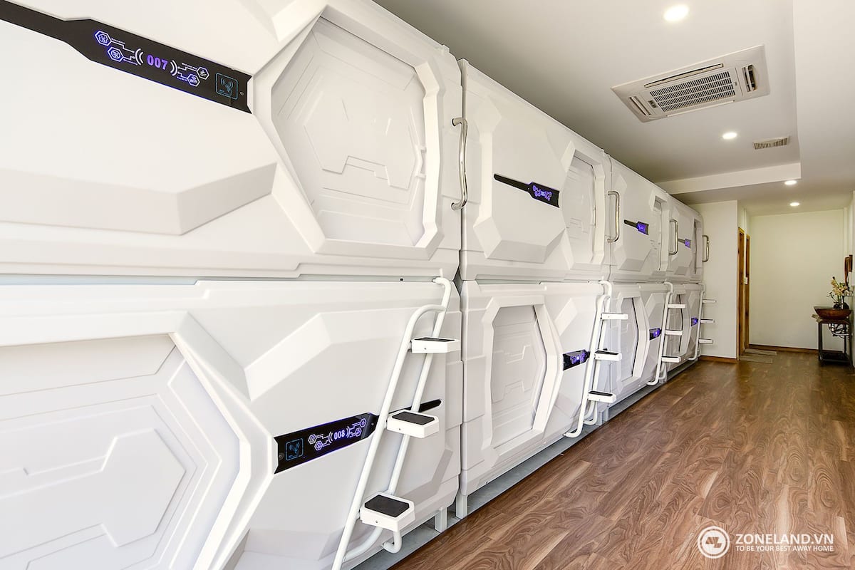 Una fila de sillones de masaje blancos y de apariencia moderna, con paneles de control, dispuestos en un pasillo con suelo de madera y un respiradero en el techo.