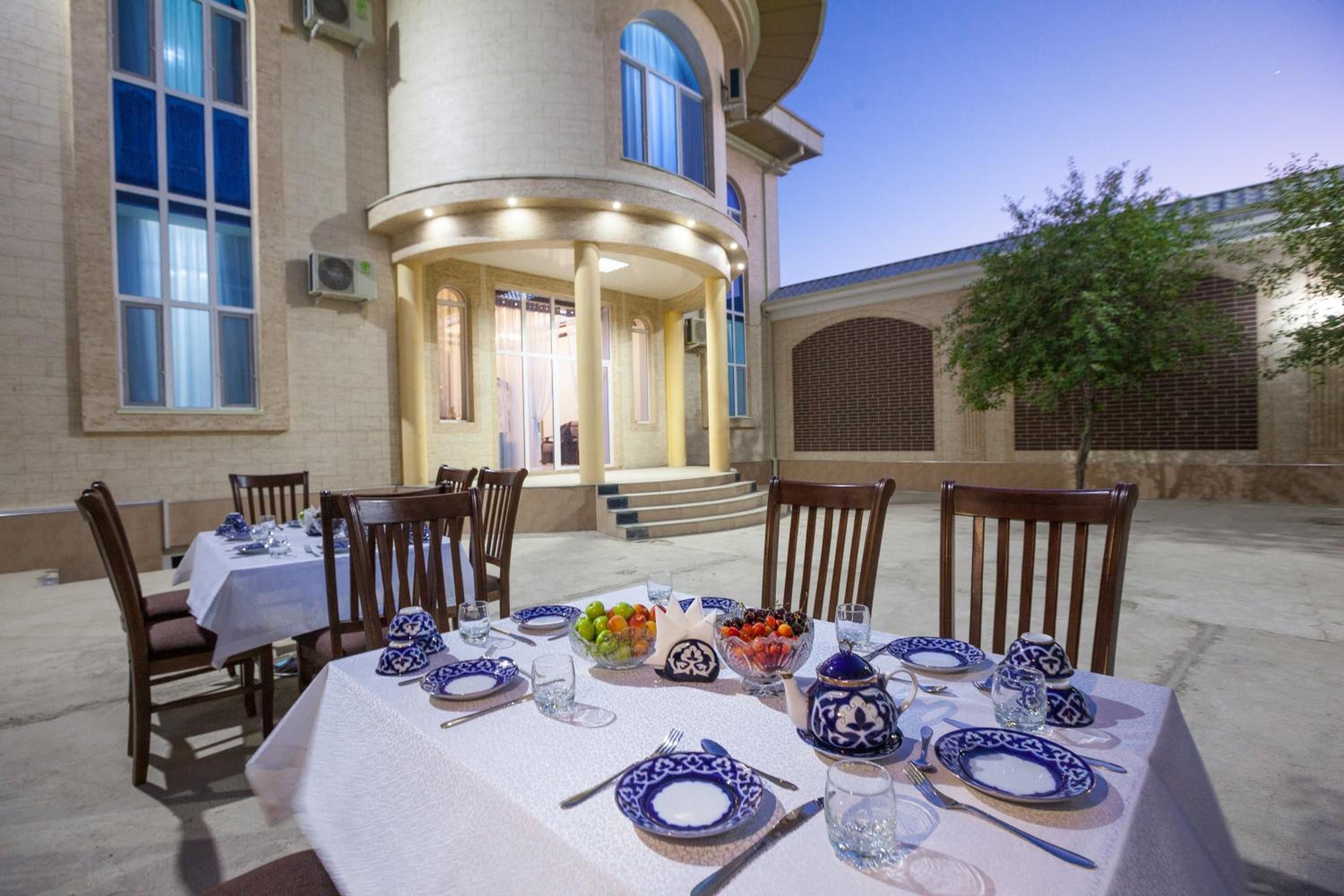 Zona d'exterior per a dinar amb taules preparades per a dues persones, amb vaixella blava i blanca, i un edifici al fons d'estil arquitectònic clàssic.