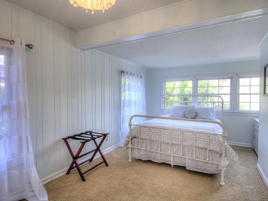 A bedroom with a white bed, a small wooden stool, and a window with curtains.