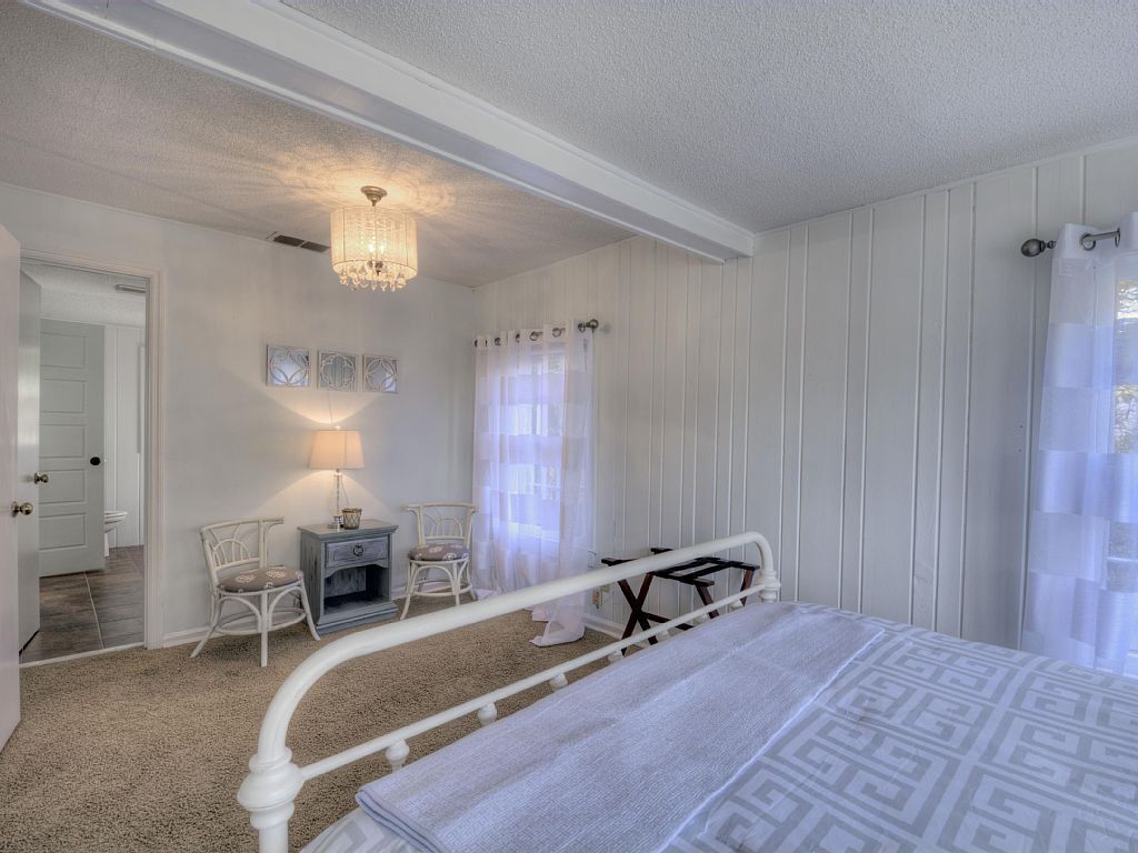 A bedroom with a bed, a nightstand, a chair, a lamp, and a chandelier.
