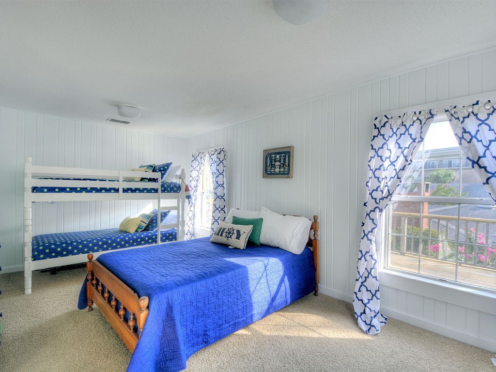 A bedroom with a bunk bed, a single bed, and a window with patterned curtains.