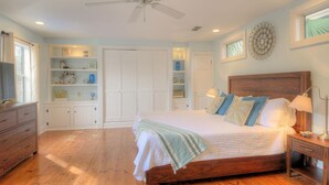 Un dormitorio con cama de madera, ventilador de techo, estanterías empotradas y una ventana con cortinas.