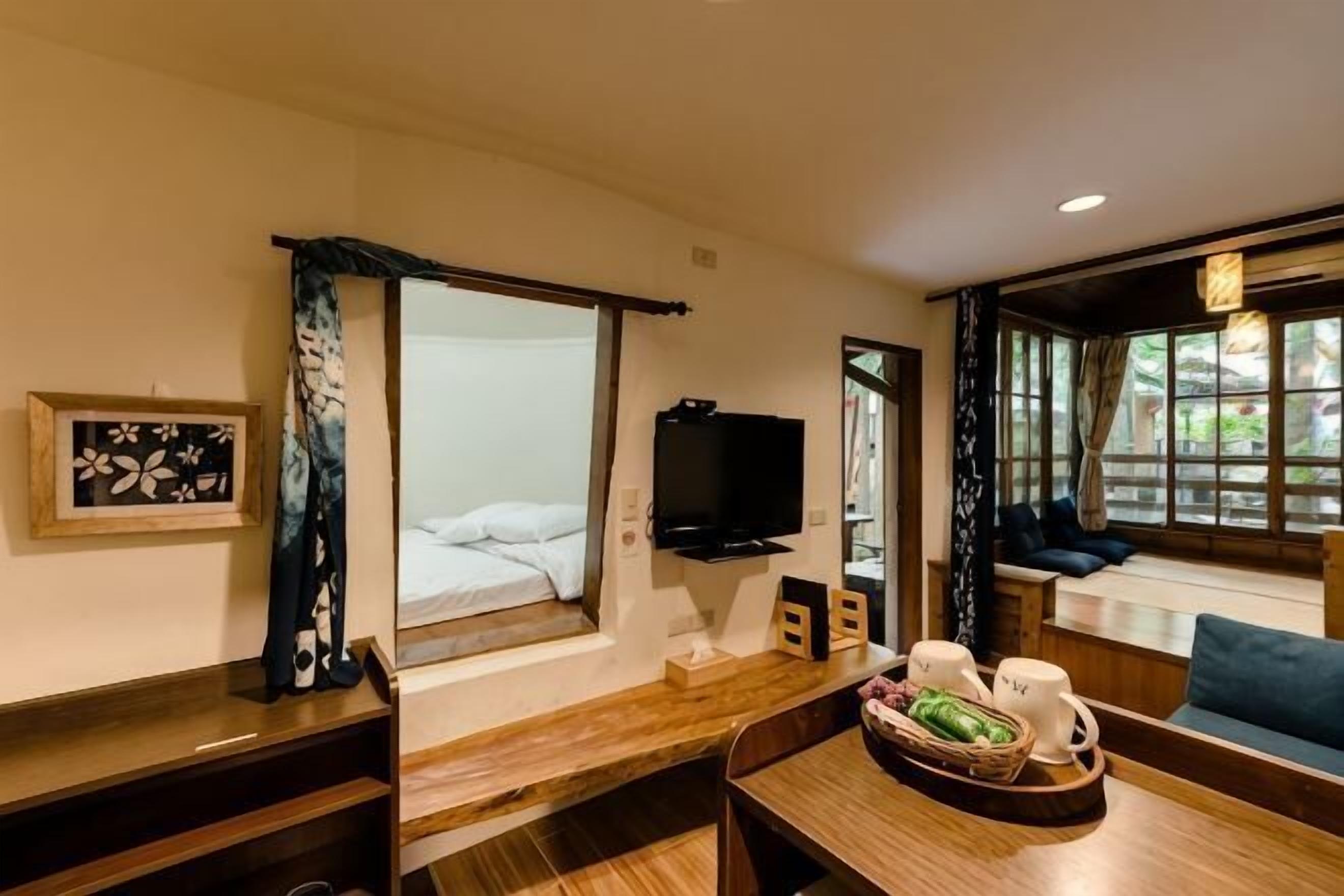 A hotel room with a bed, a TV, a dining table with chairs, a window with curtains, and a seating area with a sofa.