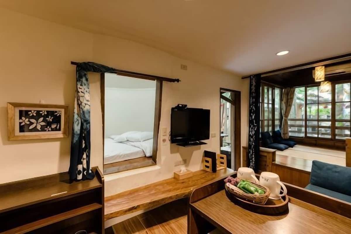 A hotel room with a bed, a TV, a dining table with chairs, a window with curtains, and a seating area with a sofa.