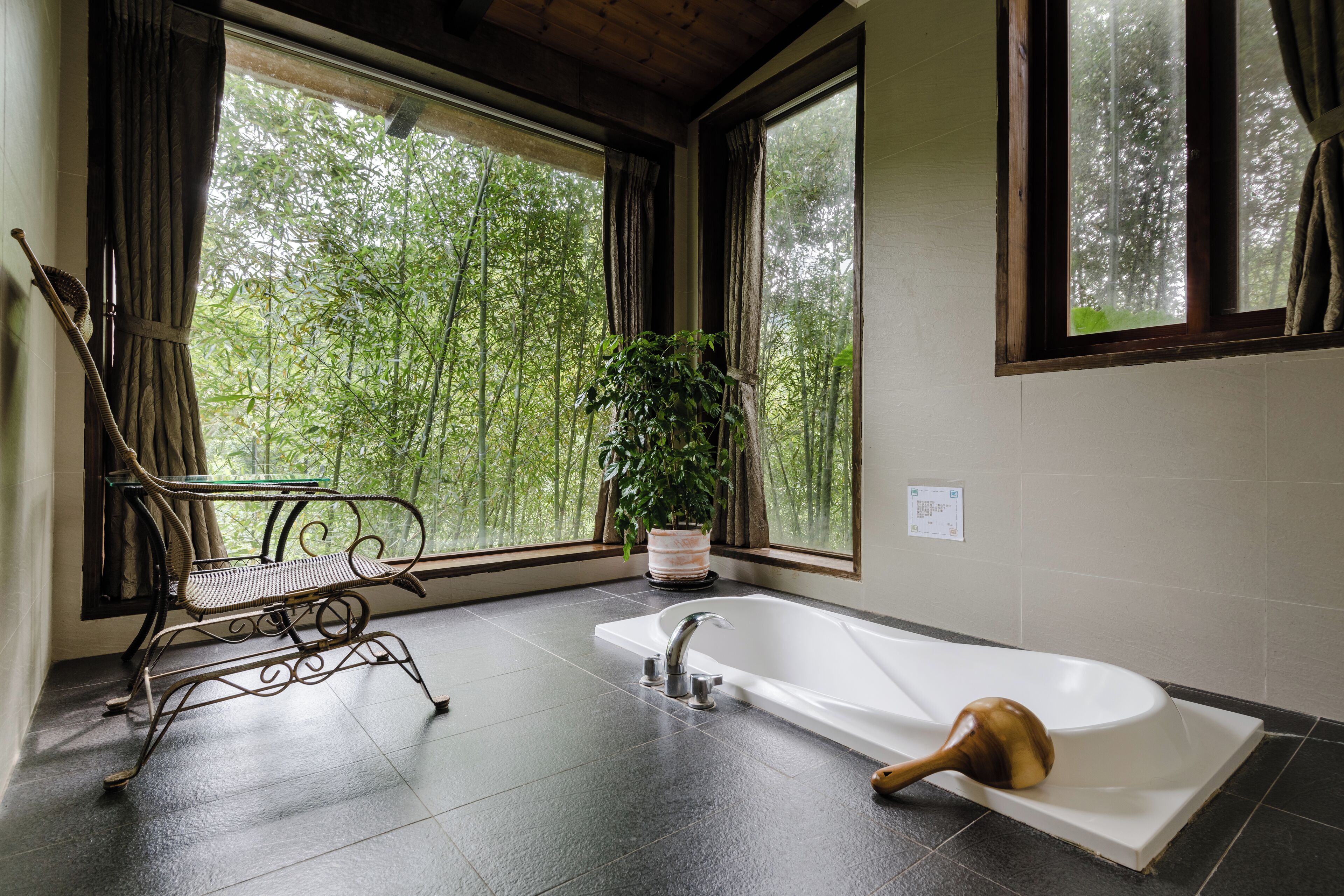 A bathroom with a bathtub, a window with a view of trees, a potted plant, and a metal bench.