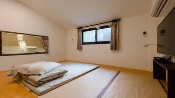 Una habitación con cama, ventana con cortinas, espejo y televisor.