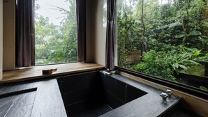 A modern bathroom with a large bathtub, a wooden bench, and a view of lush greenery outside. - Zhuo Ye Cottage (Sanyi)