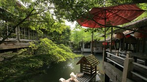 A serene riverside setting with a wooden boat docked on a bridge, surrounded by lush greenery and traditional architecture. - Zhuo Ye Cottage (Sanyi)