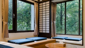 A room with a bed, a round table, and a view of trees through large windows. - Zhuo Ye Cottage (Sanyi)