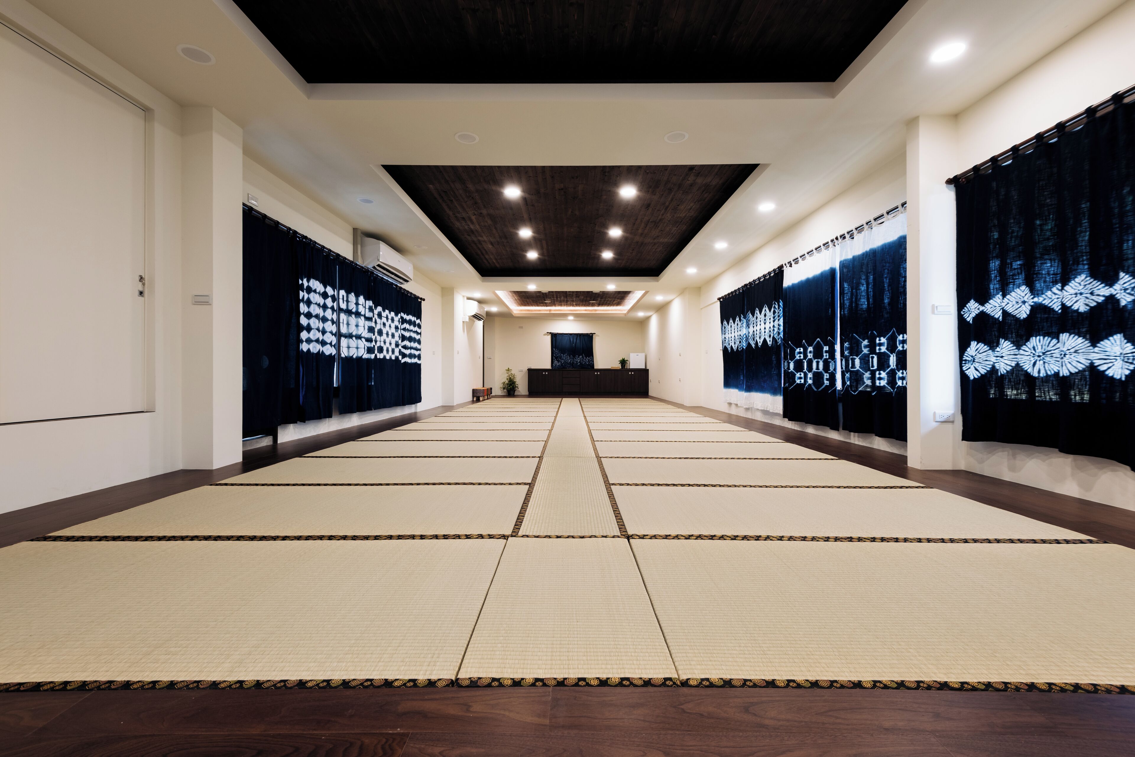 A spacious room with tatami mats, a reception desk, and a dark wooden ceiling.