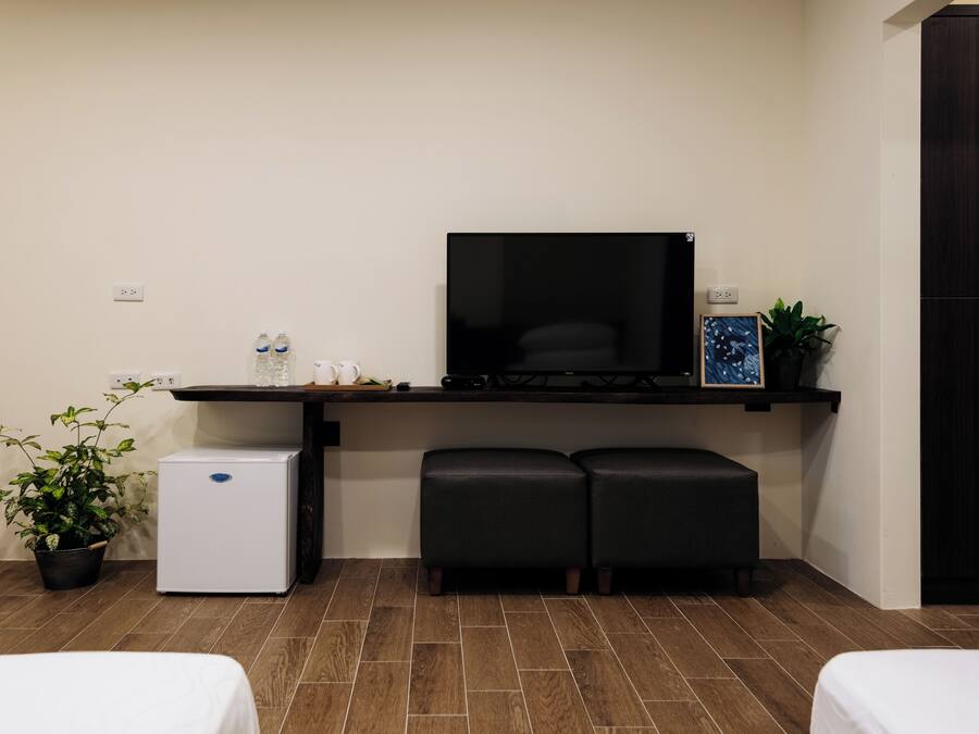 Una habitación pequeña con cama, un refrigerador, un televisor y un banco.