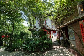 Un edificio tradicional con una escalera que lleva a una puerta roja, rodeado de abundante vegetación y faroles rojos.