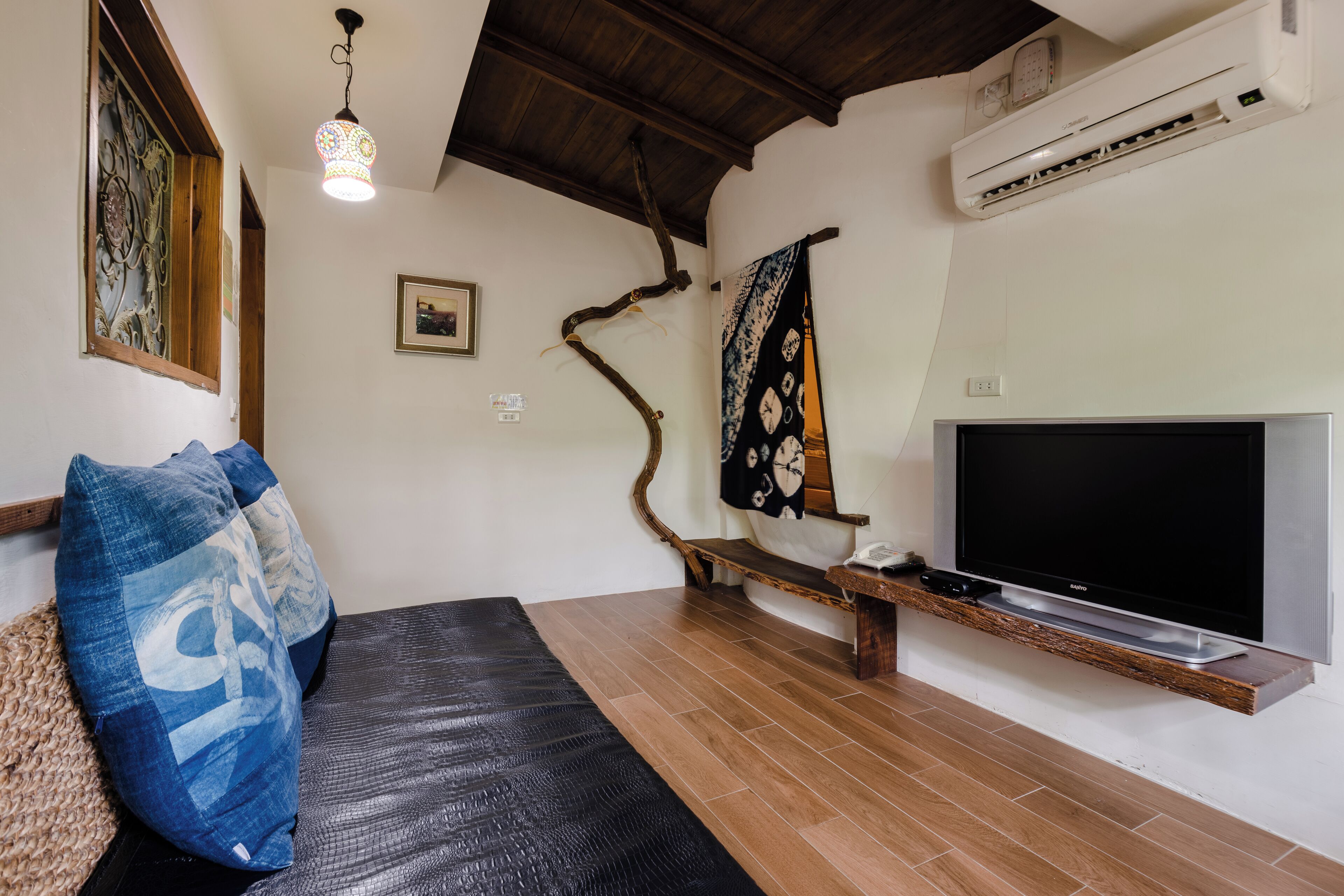 A living room with a sofa, a TV mounted on a wooden shelf, an air conditioner, and a decorative wall piece.
