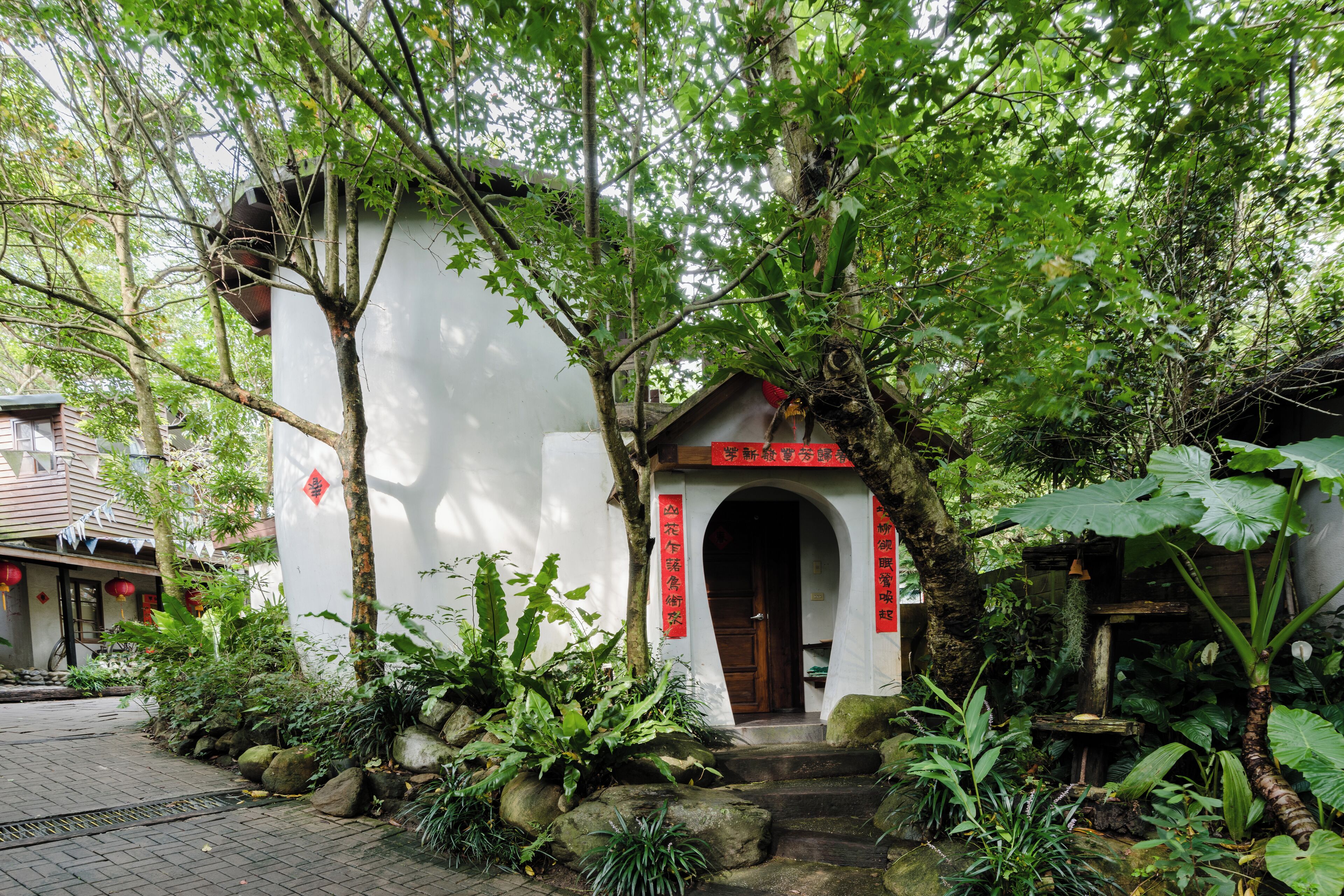 A traditional building with a wooden door and red signage, surrounded by lush greenery and rocks.