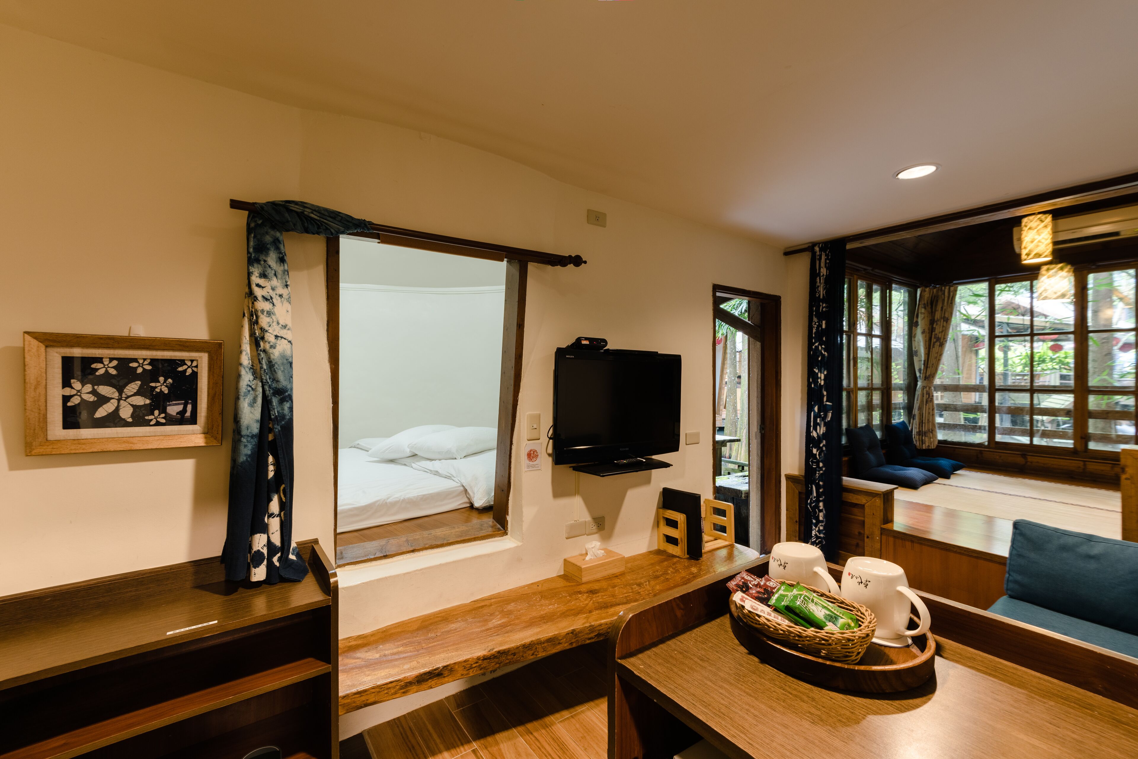 Habitación de hotel con cama, televisor, mesa de madera con una cesta y ventana con vistas.