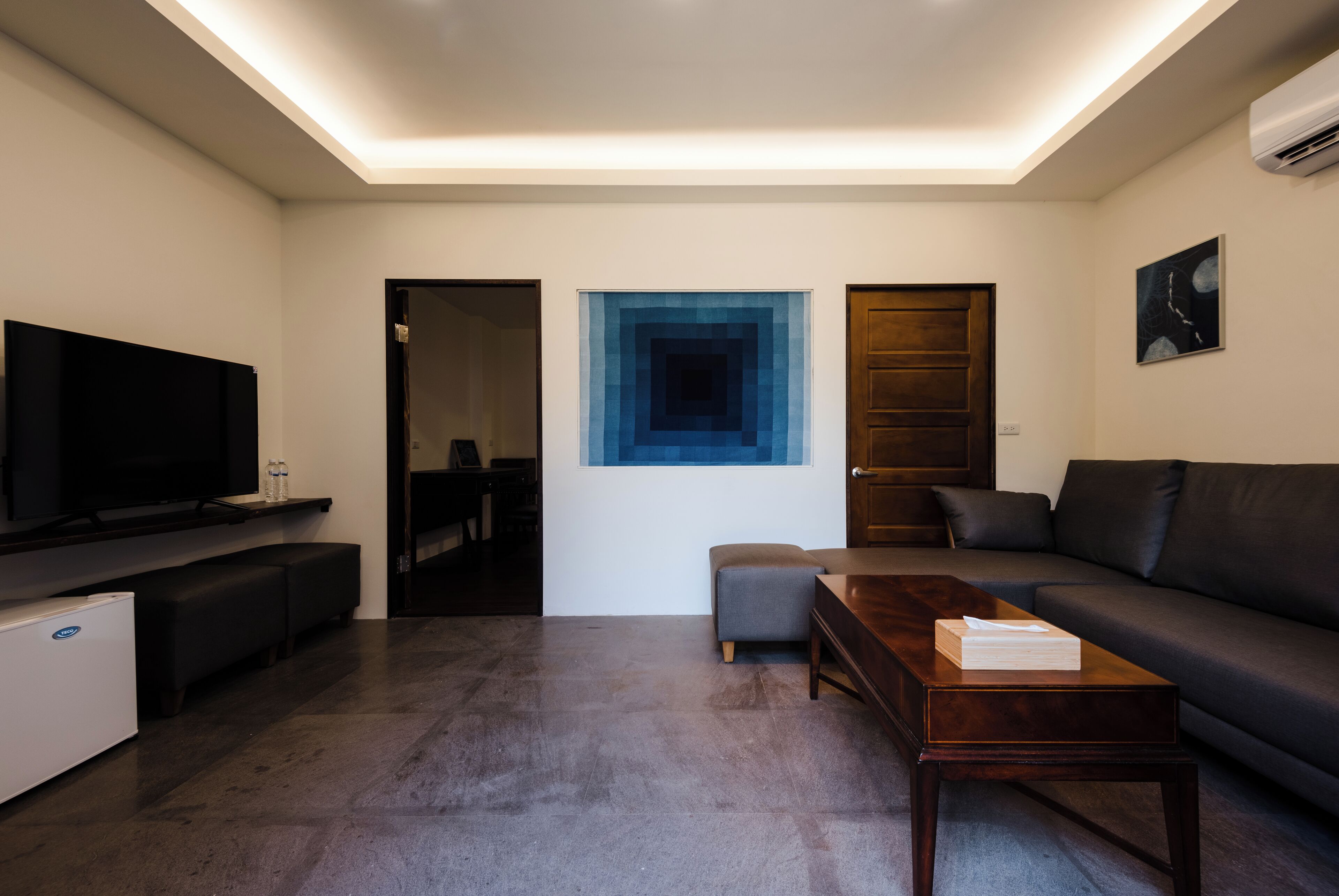 A modern living room with a flat-screen TV, a wooden coffee table, a gray sofa, and a blue accent wall.