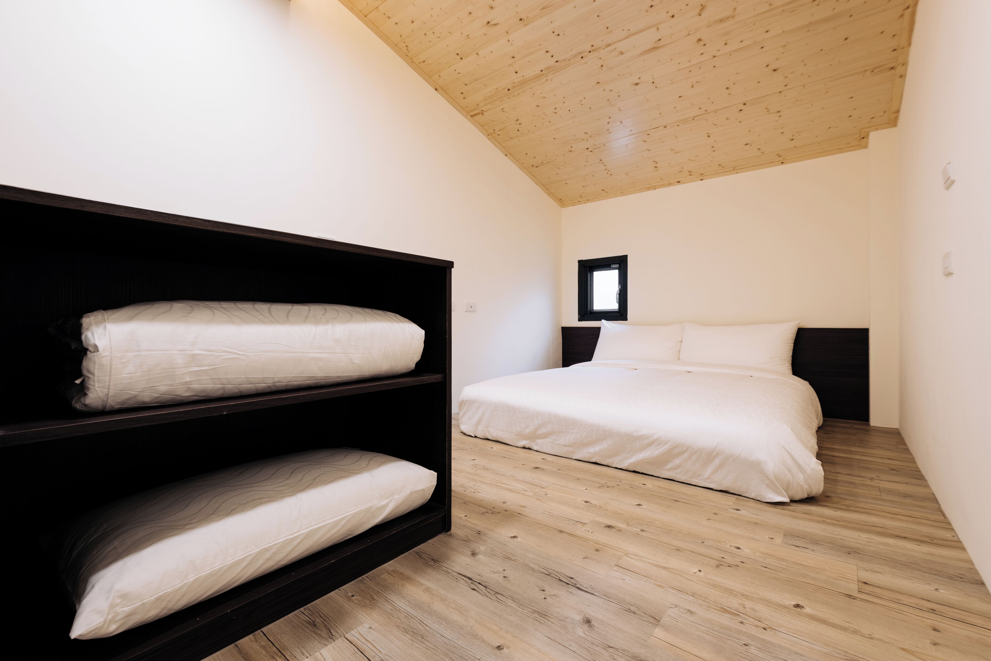 A bedroom with a bunk bed and a single bed, wooden flooring, and a sloped ceiling.