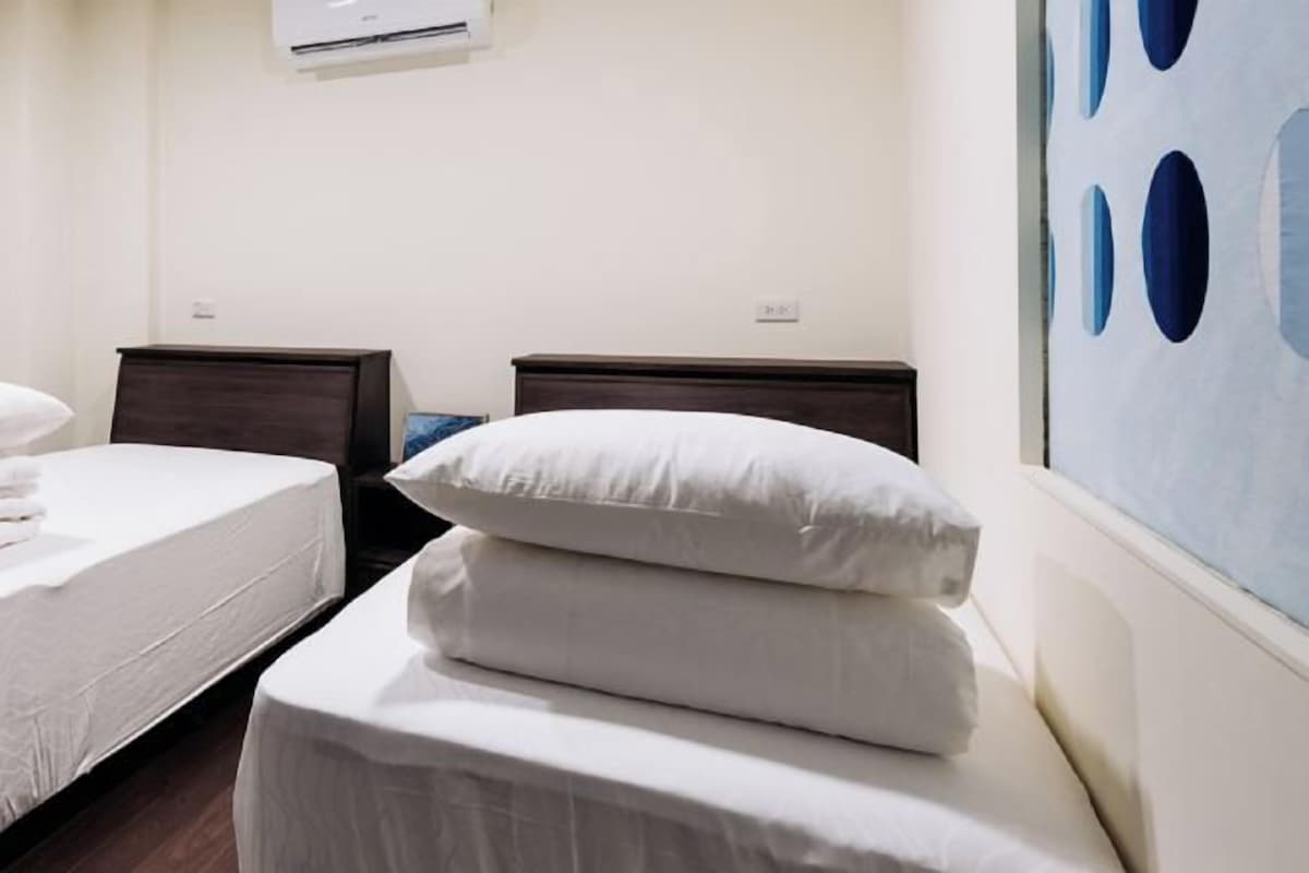 Una camera d'albergo con due letti singoli, ognuno con una testiera scura e biancheria da letto bianca.