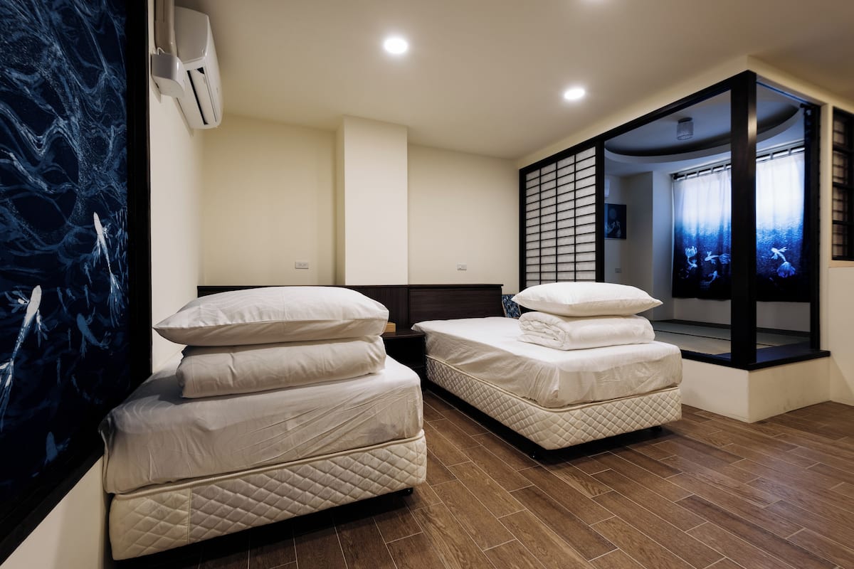 A hotel room with two beds, a large window with a view, a wall-mounted air conditioner, and a wooden floor.