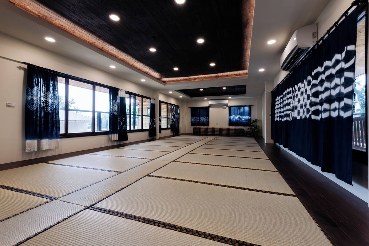 A spacious room with tatami mats, wooden beams, and large windows.