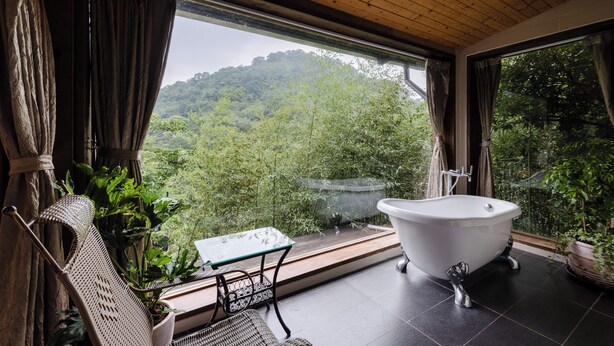A bathroom with a freestanding bathtub, a glass table, and a wicker chair. - Zhuo Ye Cottage (Sanyi)