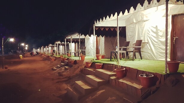 A row of tents with steps leading up to a platform, each tent has a door and a chair outside.