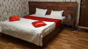A neatly made bed with white and red bedding, a wooden headboard, and a wooden floor.