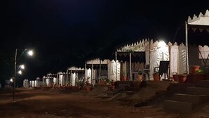 A row of tents with steps leading up to them, each with a small table and chairs.