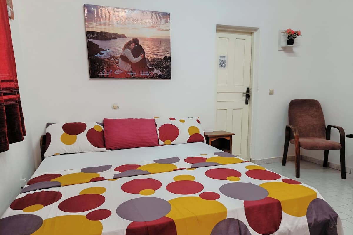 Un dormitori amb un llit, una cadira, una porta i un quadre penjat a la paret.