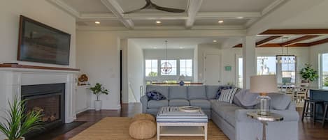 A spacious living room with a fireplace, a large sofa, and a dining area in the background.