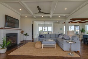 A spacious living room with a fireplace, a large sofa, and a dining area in the background.