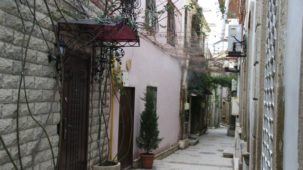 A narrow alleyway with stone walls, a small potted tree, and a metal gate. - Old East Boutiques (Baku)