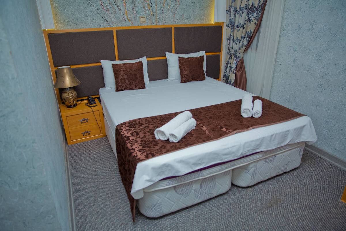 A neatly made bed with a brown bedspread, white pillows, and rolled towels.