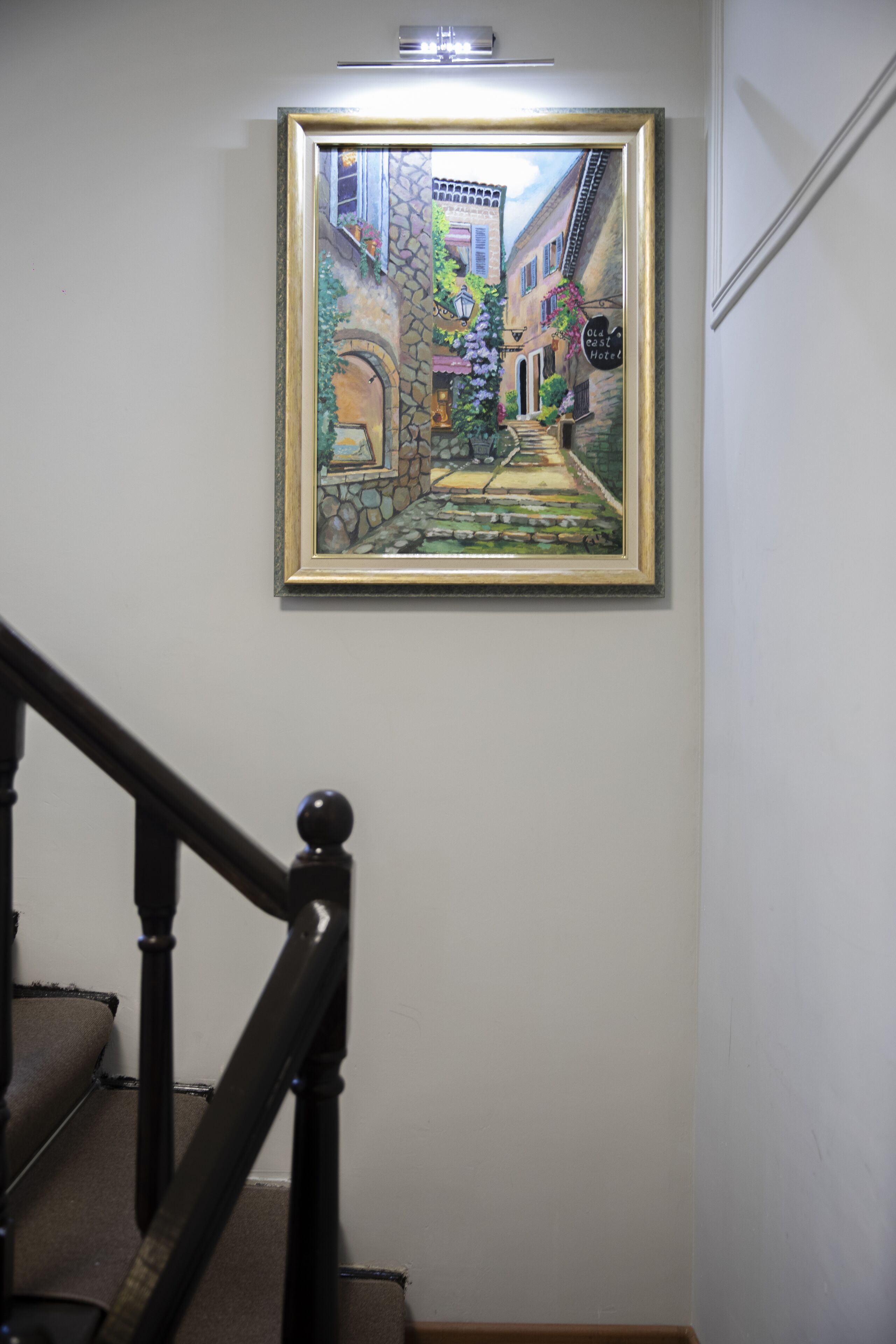 Un tableau encadré représentant une scène de rue, accroché au mur au-dessus d’un escalier.