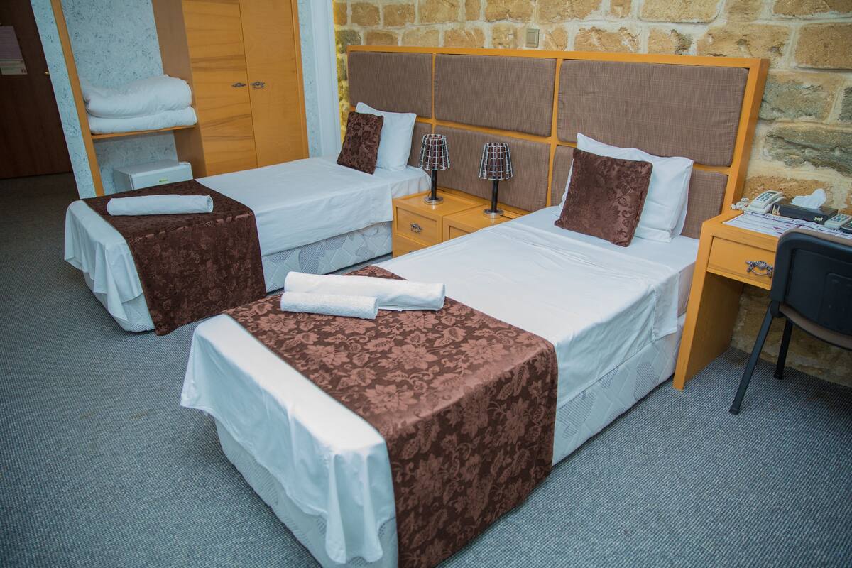 A hotel room with two single beds, a wooden headboard, a small desk with a telephone, and a chair.