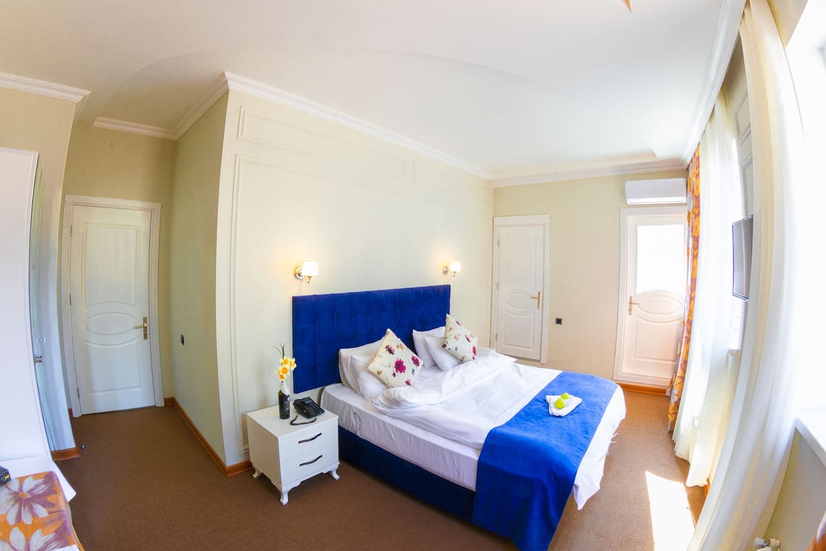 A hotel room with a large bed, a bedside table, a nightstand, and a window with curtains.