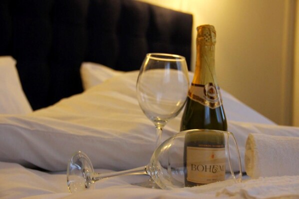 Une bouteille de vin Bohlmann et un verre à vin posés sur un lit recouvert de draps blancs.