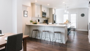 A modern kitchen with white cabinetry, a central island with stools, a microwave, and a refrigerator. - Large Home, 4 bds, 3.5 bths, complete remodeled: luxurious amenities..see pics (Cottonwood Heights)