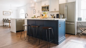 A modern kitchen with white cabinets, a central island with stools, stainless steel appliances, and a pendant light fixture. - Large Home, 4 bds, 3.5 bths, complete remodeled: luxurious amenities..see pics (Cottonwood Heights)